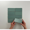 Mintgroene keramische tegels Atlas Jade Mate met handen die één tegel vasthouden