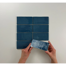 Vrouwelijke handen houden een blauwe Atlas Marine Brillo tegel boven een grid van tegels