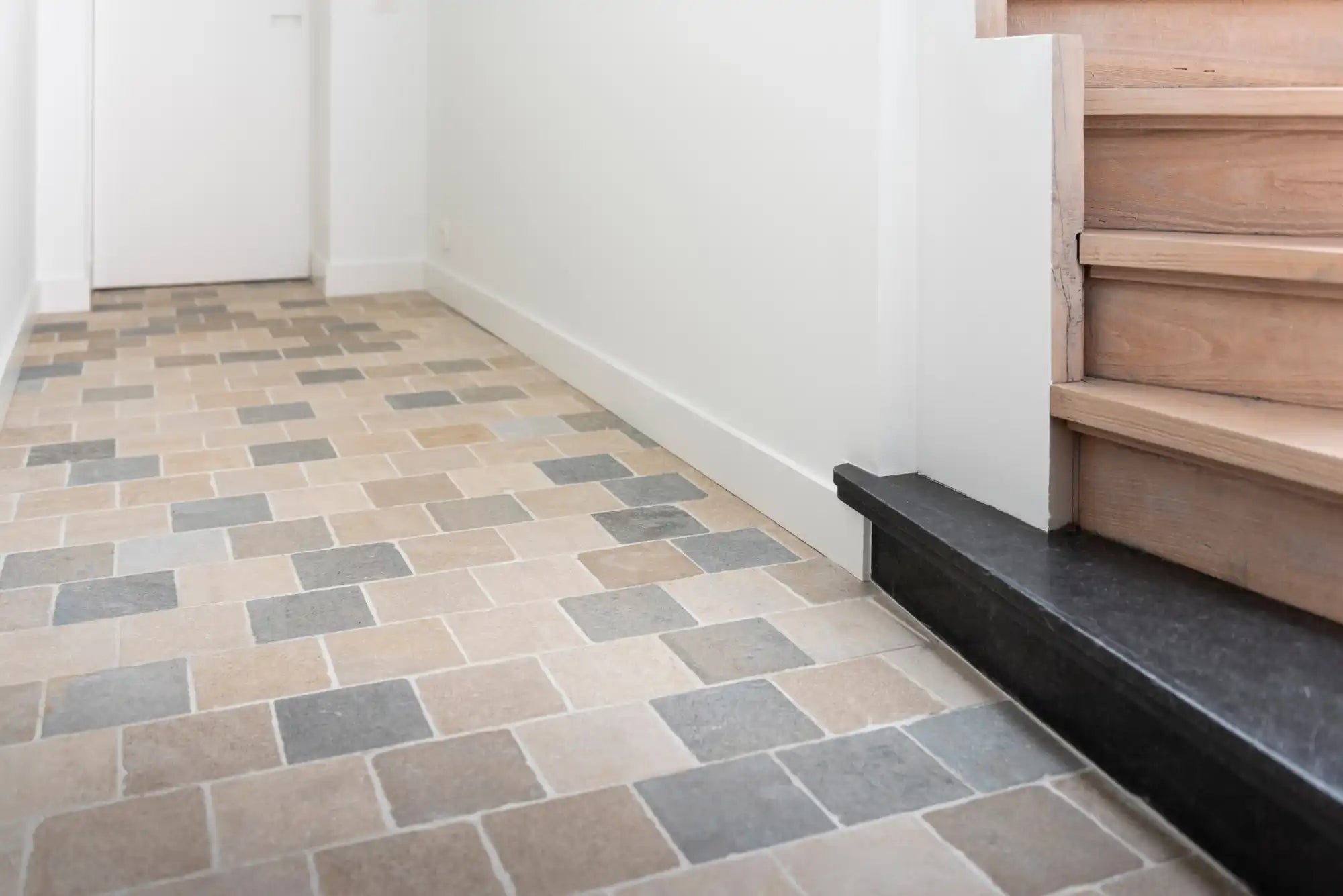 Beige en grijze mozaïektegelvloer met zwarte traploper.