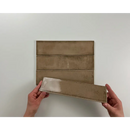 Handen met bruine keramische Alchimia Vision vloertegels in gevouwen papier