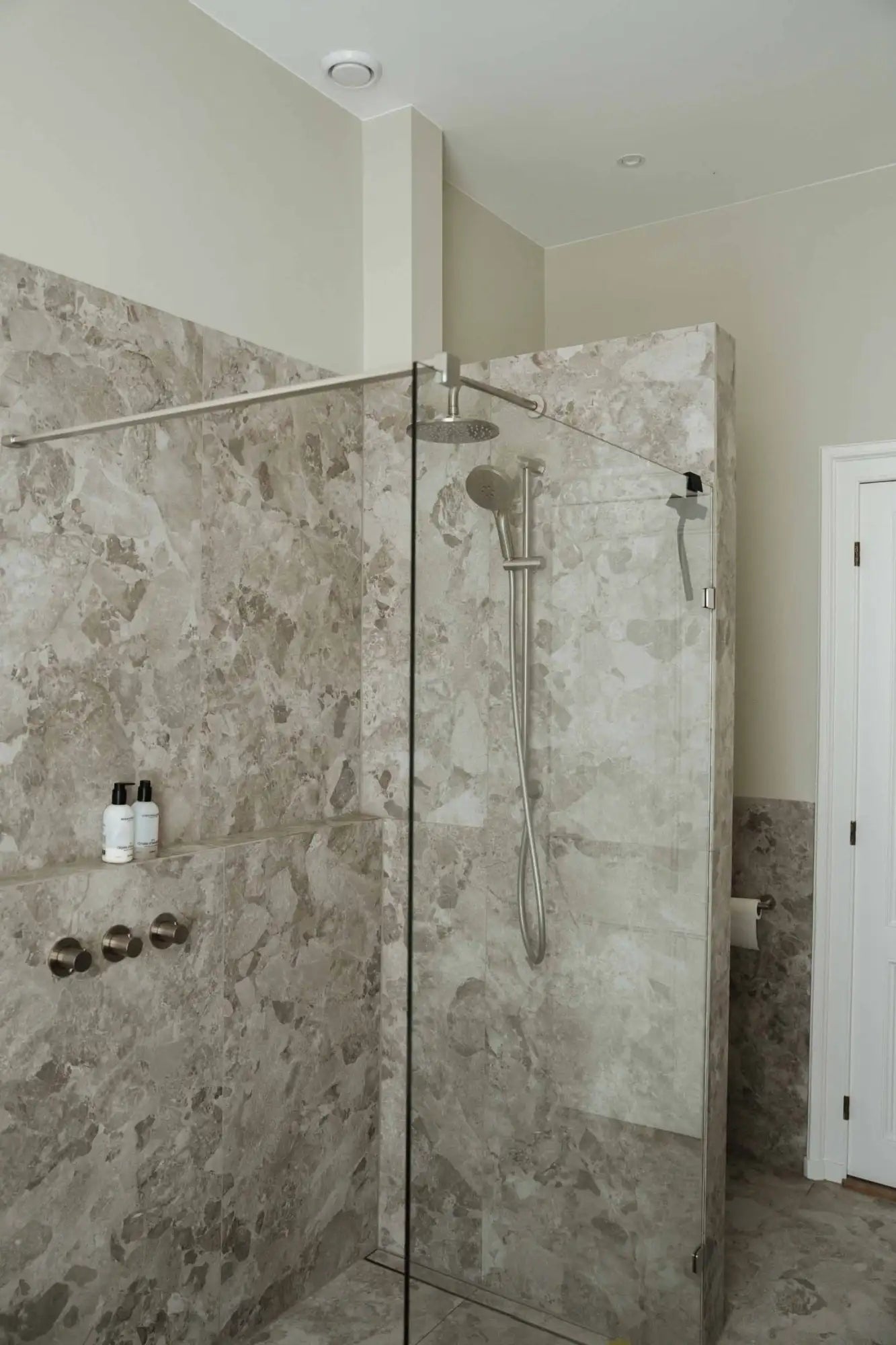 Glasdouchedeur met chroom beslag en marmeren tegelwand.