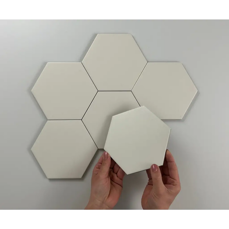 Witte hexagonale tegels in bloempatroon met handen die de Hexagon Timeless Ivory mat plaatsen