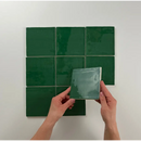 Handen die een glanzende groene tegel vasthouden tegen een muur met Oud Hollandse Witjes