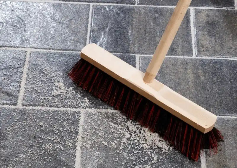 Rode bezem met houten steel en borstelharen, ontworpen voor het vegen van vloeren.