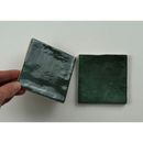 Hand houdt een donker groen glans 10x10 tegel vast met een glossy, textuur glazuur voor trend tegels donker groen