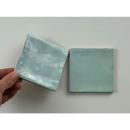 Hand houdt een trend tegels licht blauw glans 10x10 keramische tegel met een lichte blauw glans en witte motieven vast