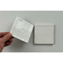 Een hand houdt een glanzende keramische witte tegel met subtiele textuur trend tegels wit glans 10x10