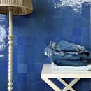 Gestapelde spijkerbroek op witte tafel tegen Zelliges Alhambra 16 Bleu Holandaise 10x10 cm muur